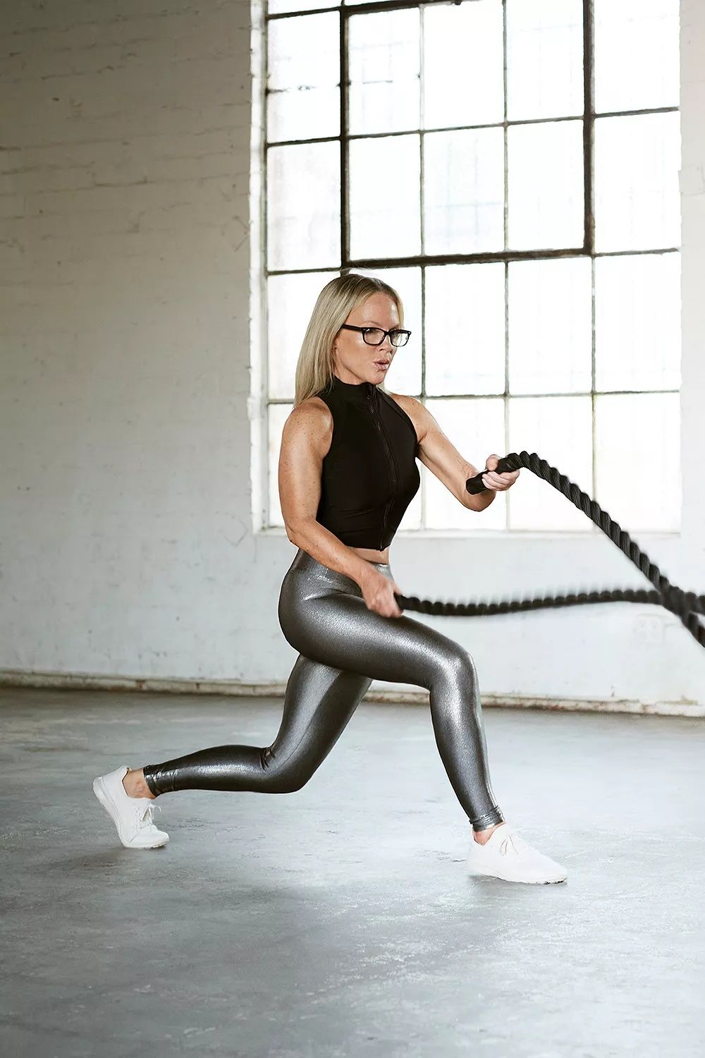 Actress Rachael Harris training with battle ropes in a black sleeveless zip top and silver metallic leggings for People Magazine, styled by Quentin Fears