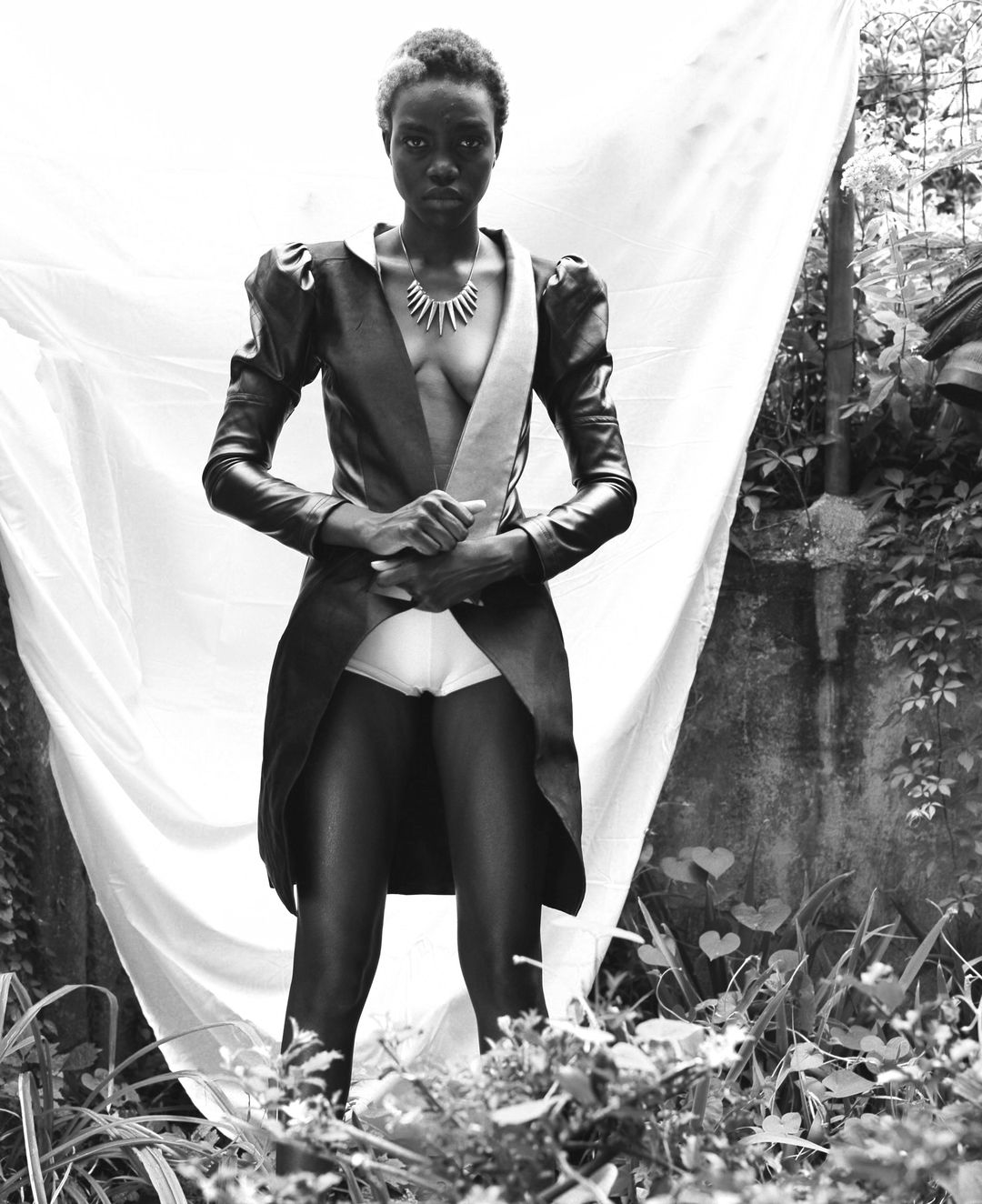 Visionarios Magazine editorial: the leather coat shot straight on against the white sheet, with the courtyard wall behind